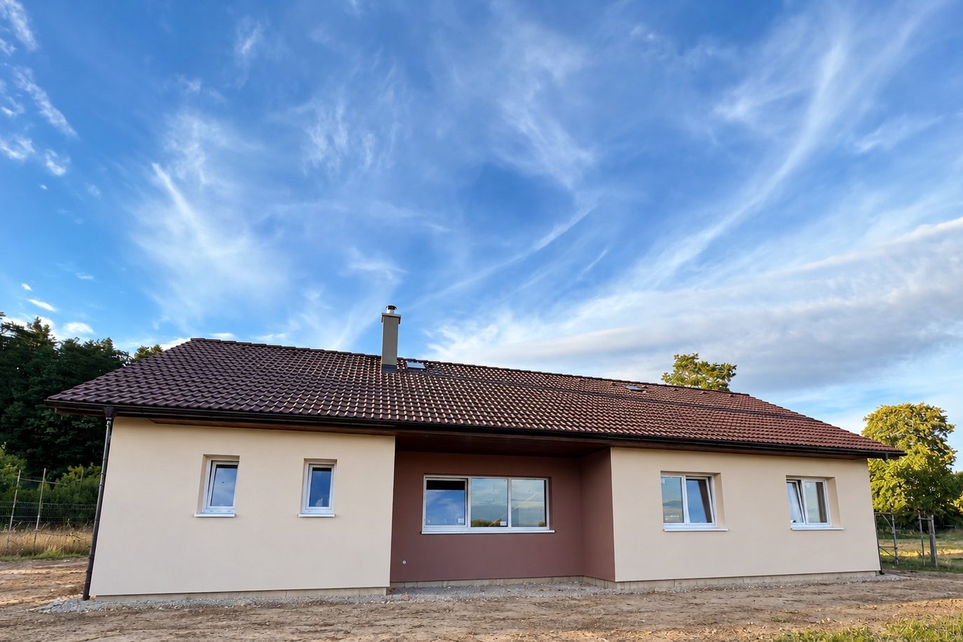 Realizace - dům s béžovou fasádou, tmavě hnědou střechou a hnědou ustoupenou částí uprostřed průčelí