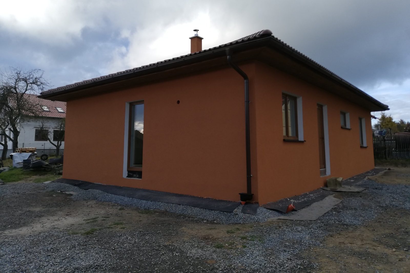 Realizace - přízemní dům s oranžovou fasádou, hnědou valbovou střechou a dřevěnými okny