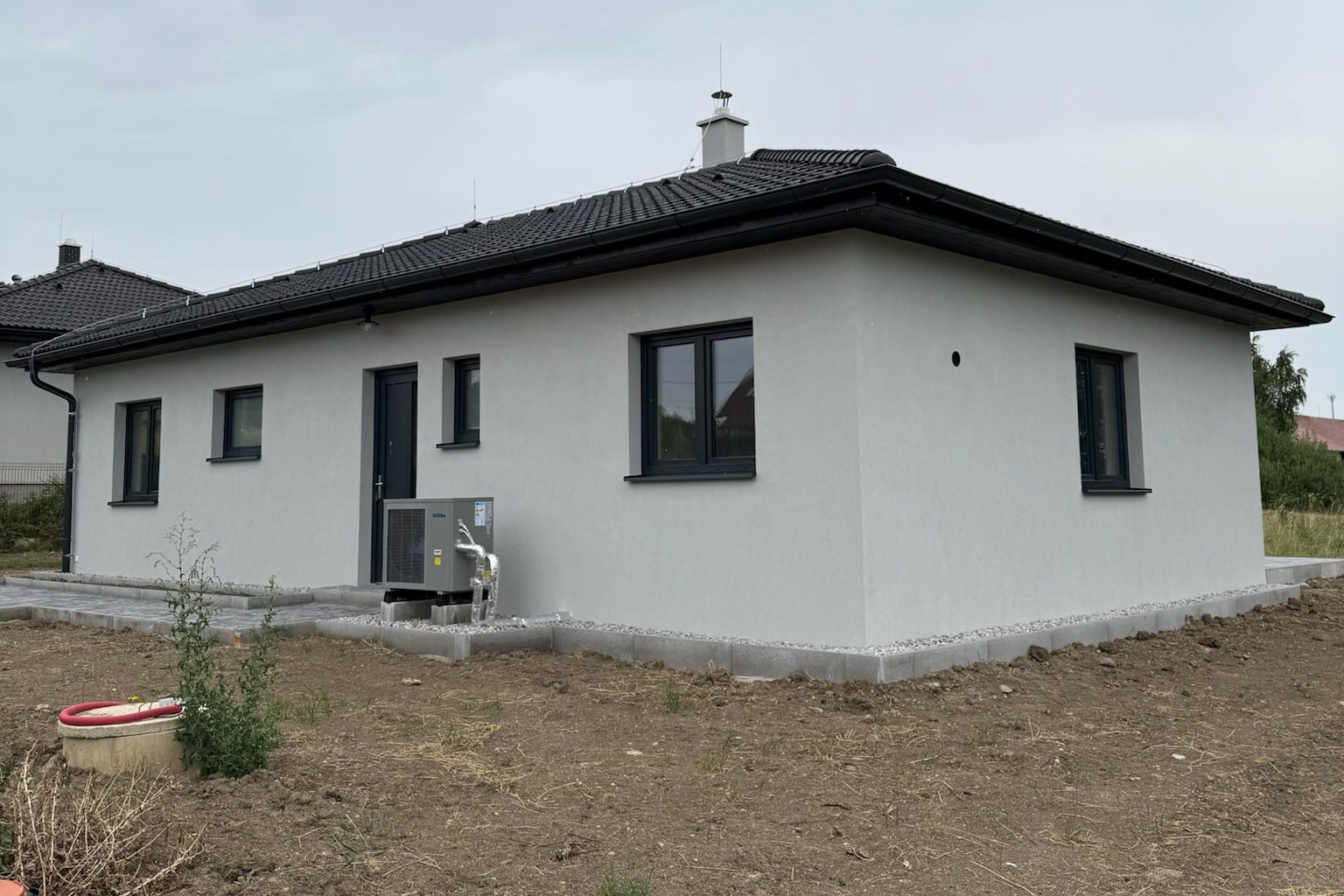 Realizace - přízemní dům se světle šedou fasádou, tmavými rámy oken a nízkou valbovou střechou