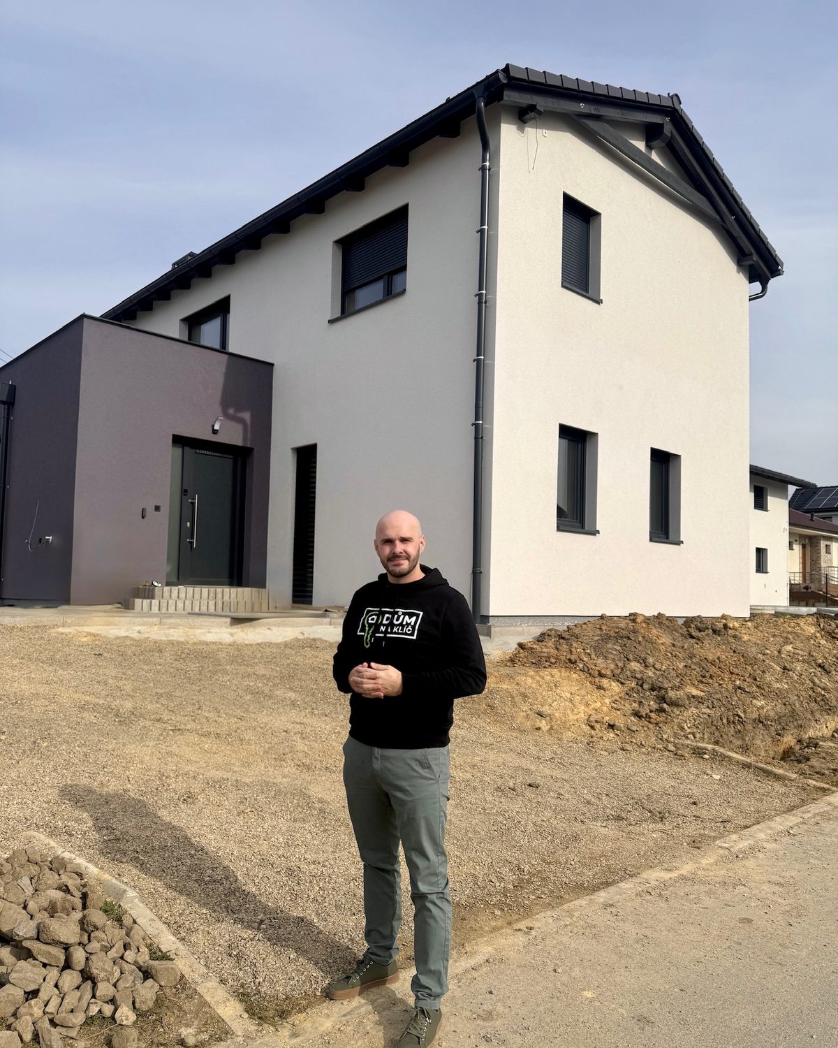 Realizace - dvoupodlažní dům se světlou fasádou, sedlovou střechou a tmavým vstupním kubusem s plochou střechou
